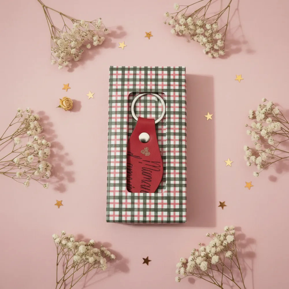 Porte-clé en cuir rouge artisanal personnalisé dans sa boîte cadeau ouverte à carreaux, décoration florale fond rose - Les Créations des A
