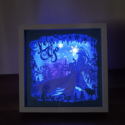 Shadow box lumineuse artisanale inspirée d'un royaume de glace enchanté. Décor multicouche avec reine de glace, flocons scintillants et paysage hivernal illuminé par des LED multicolores - Les Créations des A