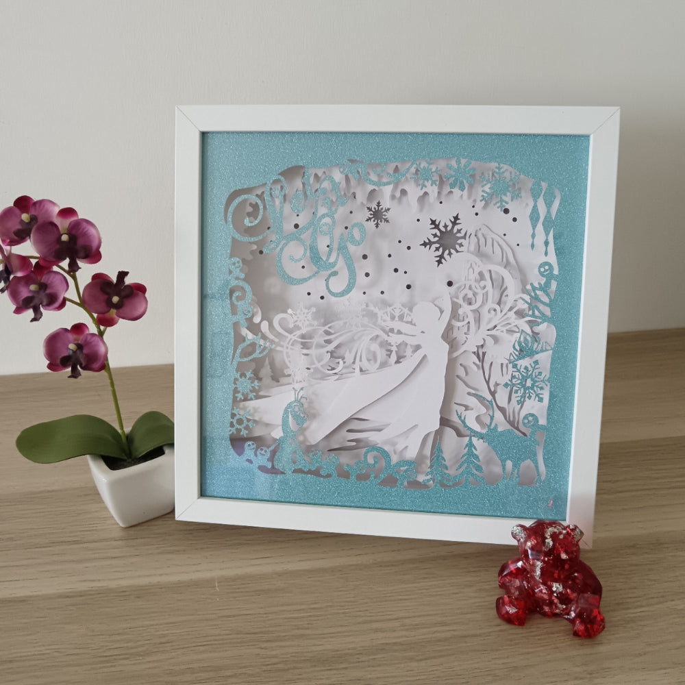 Shadow box lumineuse artisanale inspirée d'un royaume de glace enchanté. Décor multicouche avec reine de glace, flocons scintillants et paysage hivernal illuminé par des LED multicolores - Les Créations des A
