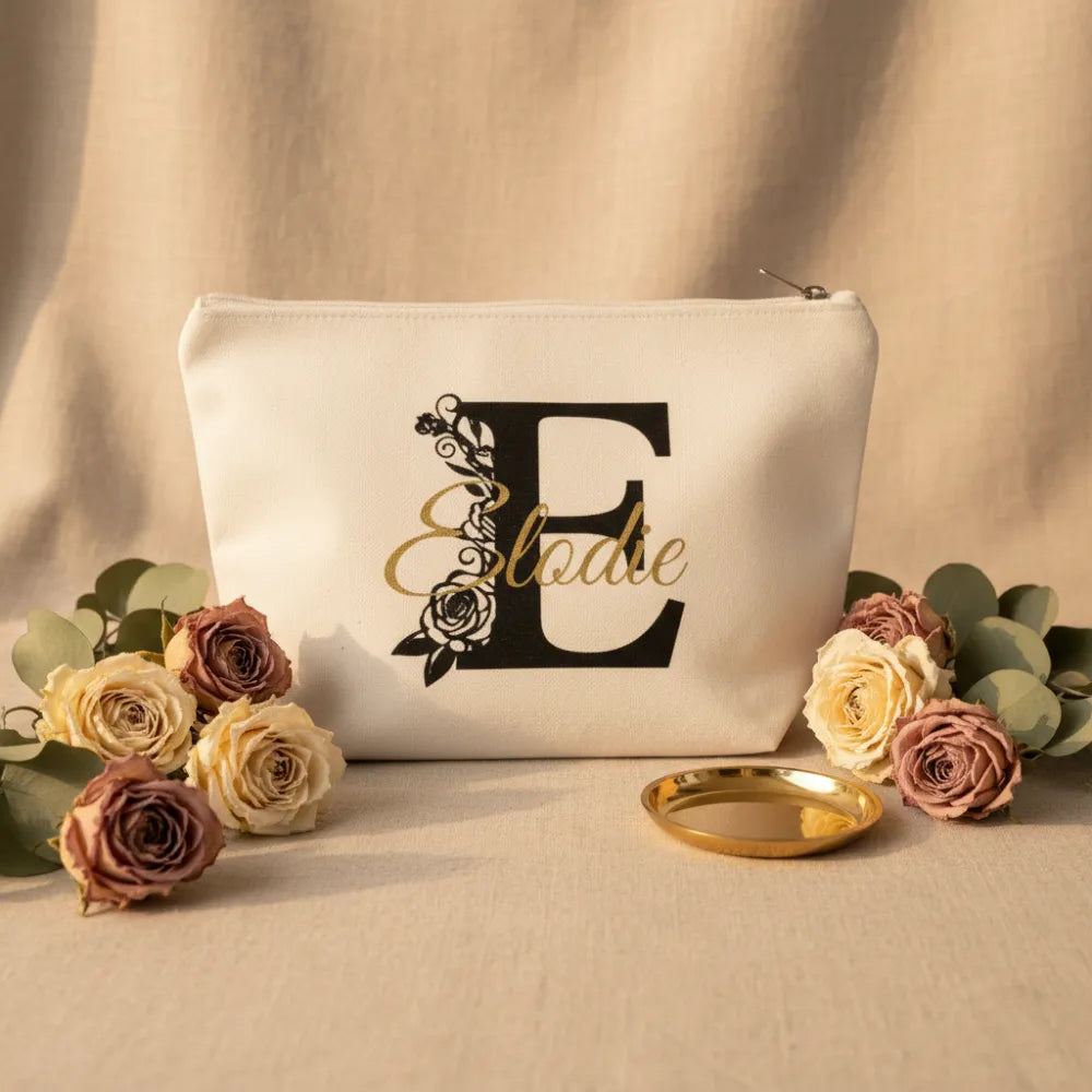 Pochette toile blanche personnalisée lettre florale E et prénom Elodie, posée sur lin beige avec roses séchées et feuilles d'eucalyptus - Les Créations des A
