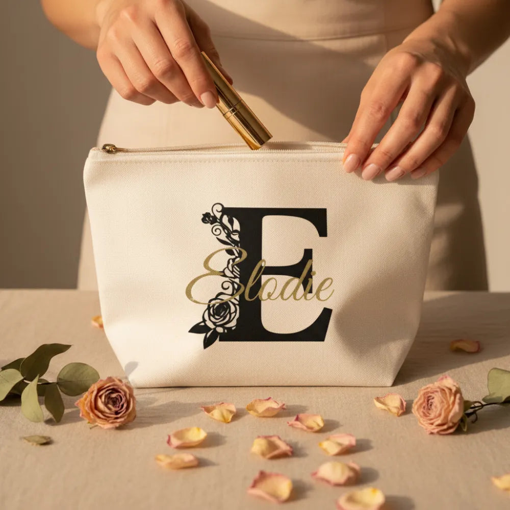 Mains féminines ouvrant une pochette toile blanche personnalisée avec lettre florale E et prénom Elodie en script doré - Les Créations des A