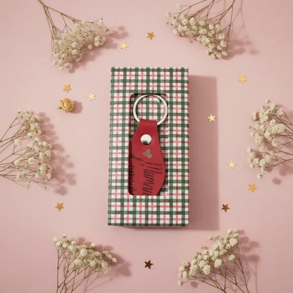 Porte-clé en cuir rouge artisanal personnalisé dans sa boîte cadeau ouverte à carreaux, décoration florale fond rose - Les Créations des A
