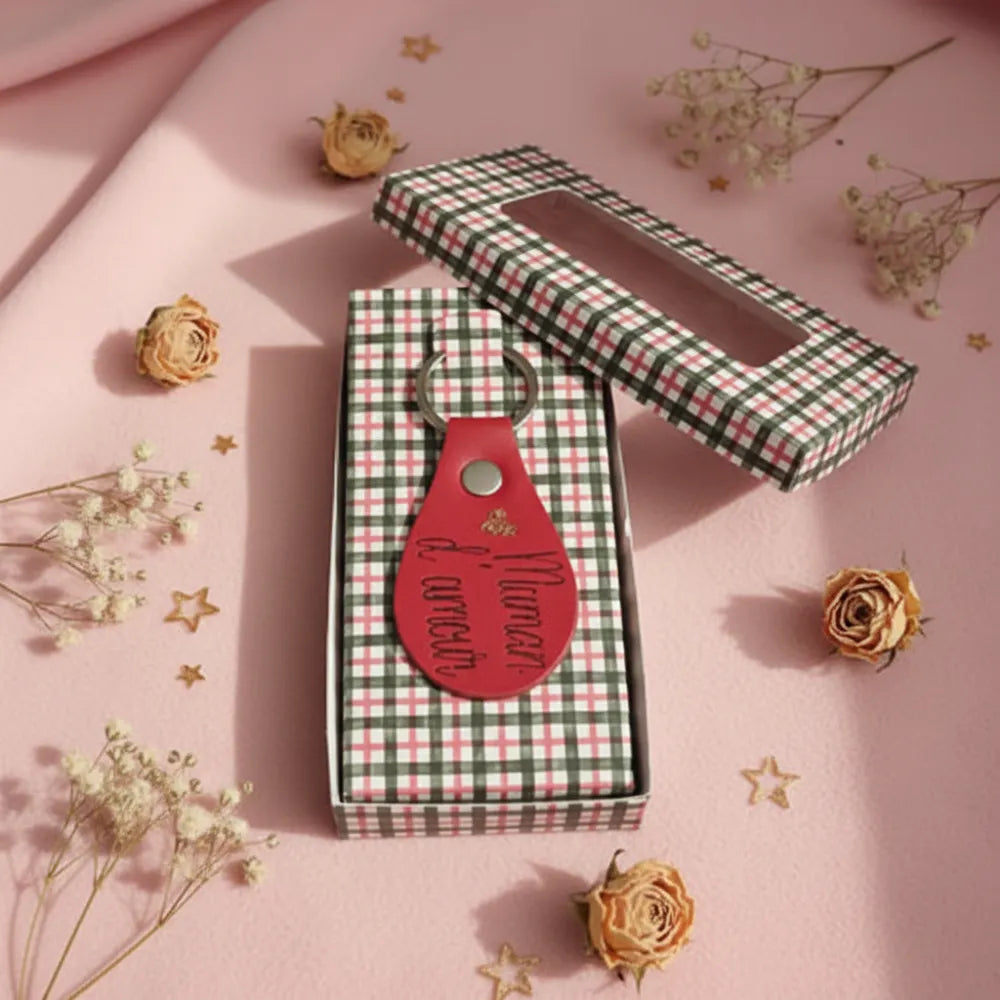 Porte-clé en cuir rouge posé sur sa boîte cadeau à carreaux verte et blanche, fond rose poudré fleurs séchées - Les Créations des A