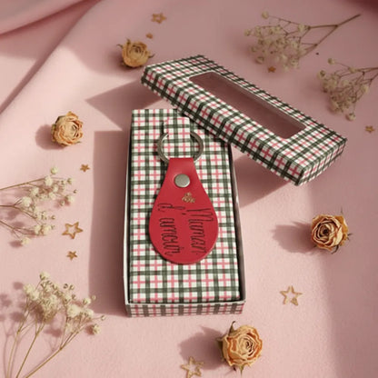Porte-clé en cuir rouge posé sur sa boîte cadeau à carreaux verte et blanche, fond rose poudré fleurs séchées - Les Créations des A