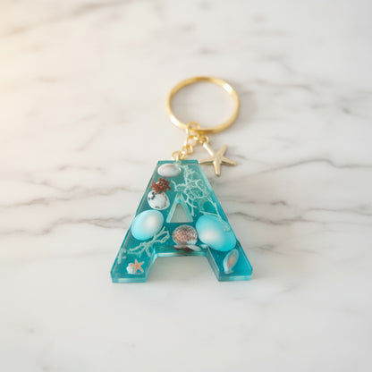 Porte-clé lettre A en résine époxy thème océan avec coquillages naturels et effet vague bleu turquoise, fabrication artisanale.  - Les Créations des A