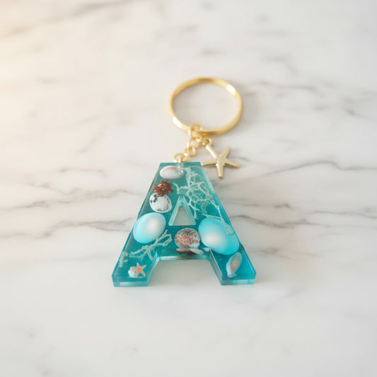 Porte-clé lettre A en résine époxy thème océan avec coquillages naturels et effet vague bleu turquoise, fabrication artisanale.  - Les Créations des A