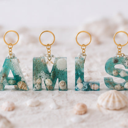 Porte-clés personnalisés en résine époxy thème océan avec coquillages naturels et mousse blanche sur fond sable - Les Créations des A