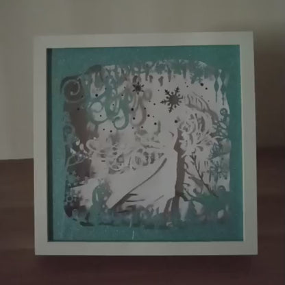 Shadow box lumineuse artisanale inspirée d'un royaume de glace enchanté. Décor multicouche avec reine de glace, flocons scintillants et paysage hivernal illuminé par des LED multicolores - Les Créations des A
