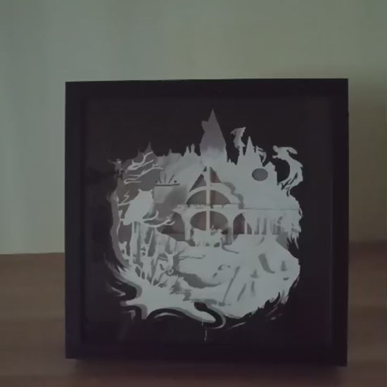 Shadow box lumineuse artisanale inspirée d'un univers de sorciers. Décor multicouche représentant un château magique, un train légendaire et plusieurs éléments fantastiques avec éclairage LED multicolore - Les Créations des A