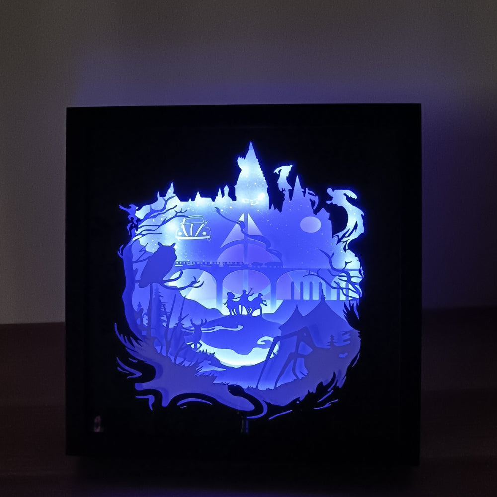 Shadow box lumineuse artisanale inspirée d'un univers de sorciers. Décor multicouche représentant un château magique, un train légendaire et plusieurs éléments fantastiques avec éclairage LED multicolore - Les Créations des A