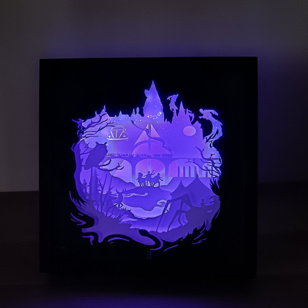 Shadow box lumineuse artisanale inspirée d'un univers de sorciers. Décor multicouche représentant un château magique, un train légendaire et plusieurs éléments fantastiques avec éclairage LED multicolore - Les Créations des A