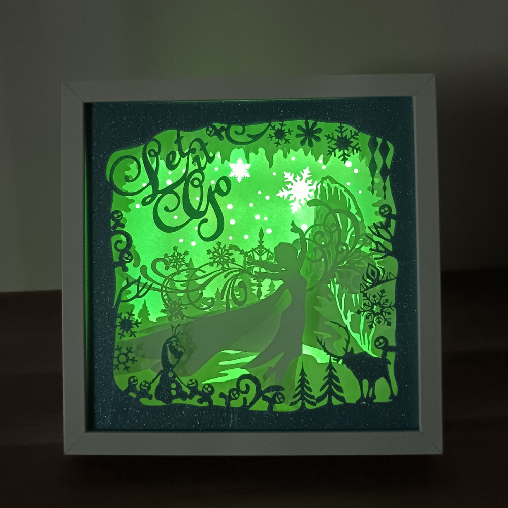 Shadow box lumineuse artisanale inspirée d'un royaume de glace enchanté. Décor multicouche avec reine de glace, flocons scintillants et paysage hivernal illuminé par des LED multicolores - Les Créations des A