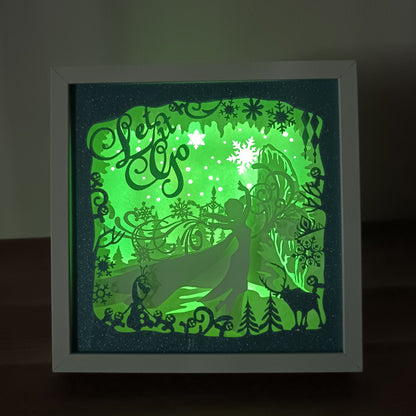 Shadow box lumineuse artisanale inspirée d'un royaume de glace enchanté. Décor multicouche avec reine de glace, flocons scintillants et paysage hivernal illuminé par des LED multicolores - Les Créations des A