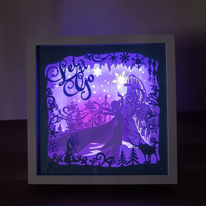 Shadow box lumineuse artisanale inspirée d'un royaume de glace enchanté. Décor multicouche avec reine de glace, flocons scintillants et paysage hivernal illuminé par des LED multicolores - Les Créations des A