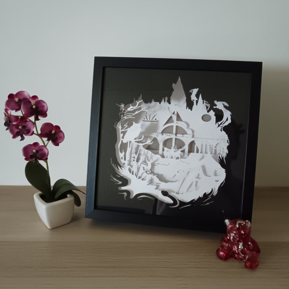 Shadow box lumineuse artisanale inspirée d'un univers de sorciers. Décor multicouche représentant un château magique, un train légendaire et plusieurs éléments fantastiques avec éclairage LED multicolore - Les Créations des A