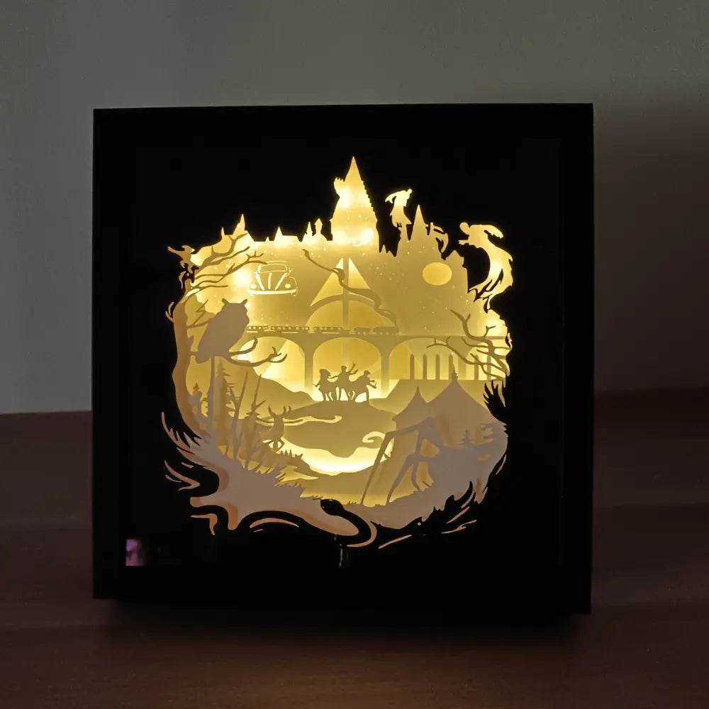 Shadow box lumineuse artisanale inspirée d'un univers de sorciers. Décor multicouche représentant un château magique, un train légendaire et plusieurs éléments fantastiques avec éclairage LED multicolore - Les Créations des A