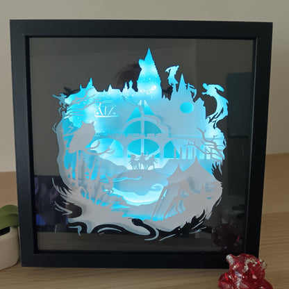 Shadow box lumineuse artisanale inspirée d'un univers de sorciers. Décor multicouche représentant un château magique, un train légendaire et plusieurs éléments fantastiques avec éclairage LED multicolore - Les Créations des A