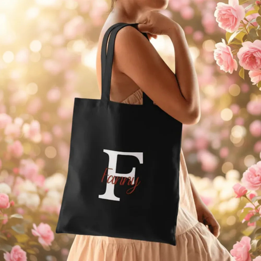 Femme portant un tote bag noir avec initiale "F" et prénom Fanny dans un jardin fleuri – cadeau original personnalisé - Les Créations des A